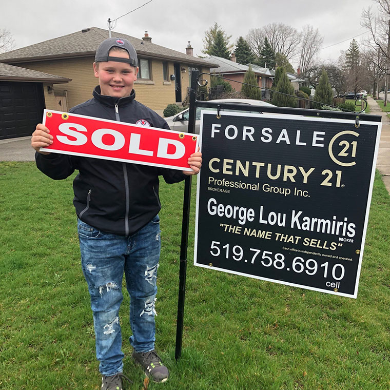 Teenager holding sold sign on front lawn.