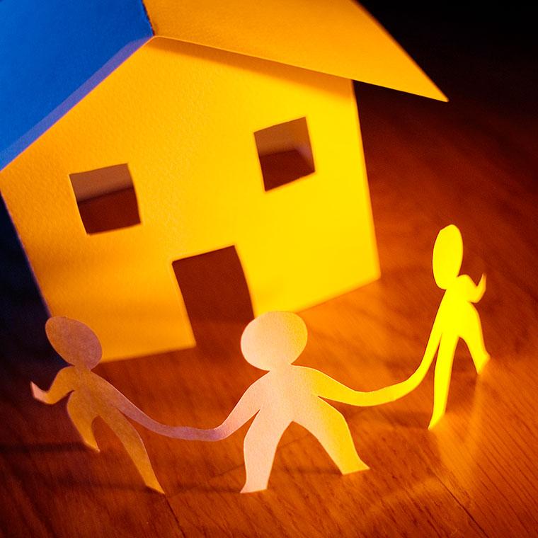 Paper cut-outs of people in circle around a small model of a house to signify community.